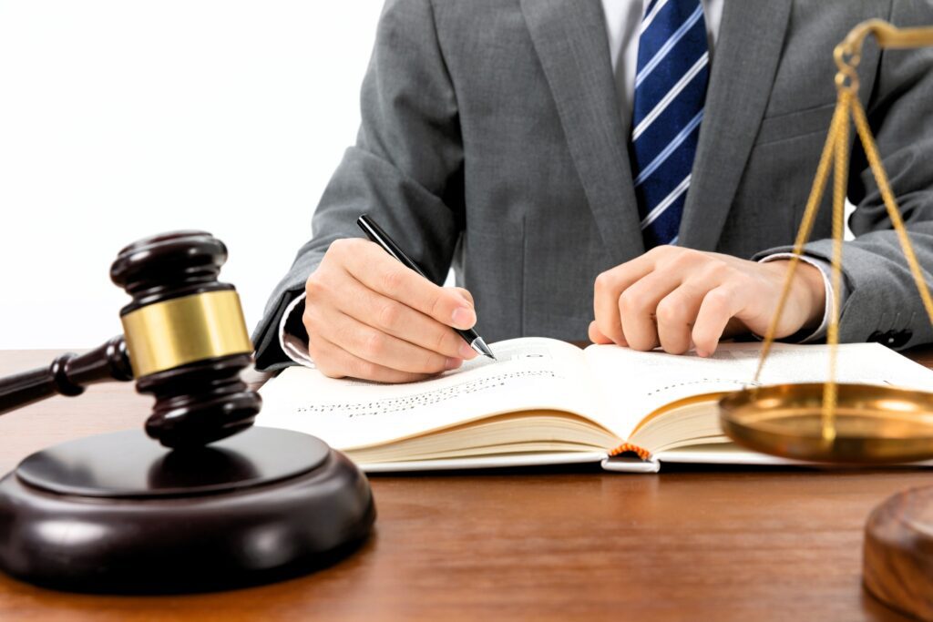 Close-up of a legal professional writing in a book with gavel and justice scales on desk, symbolizing UAE legal translator certification process, notary regulations, and Ministry of Justice compliance for aspiring legal translators in the UAE.